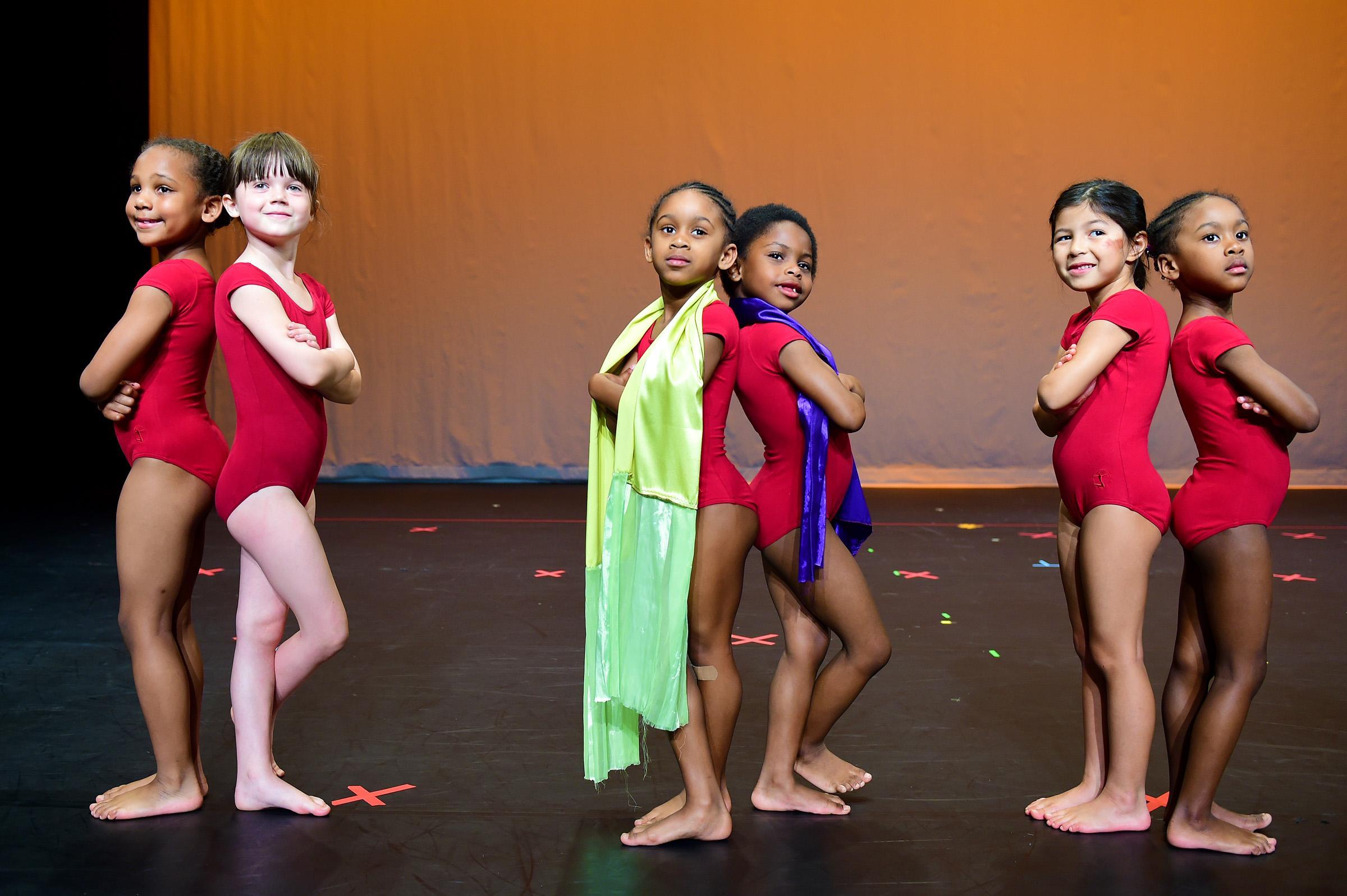 6 little girls pose back to back on stage in red leotards