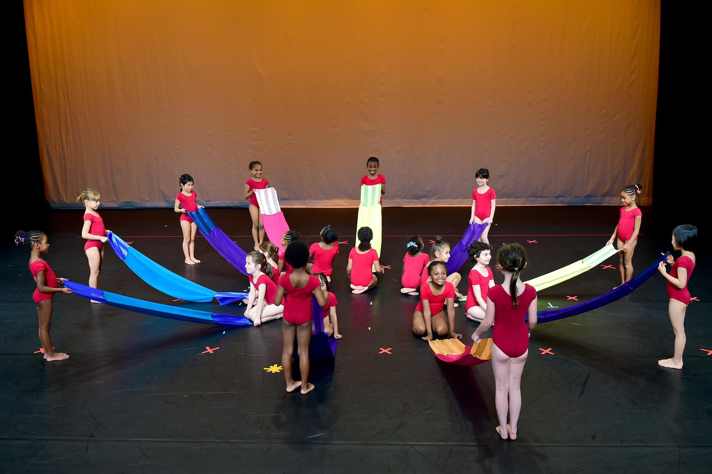 Little girls in red leotards play with parachute ribbons on stage