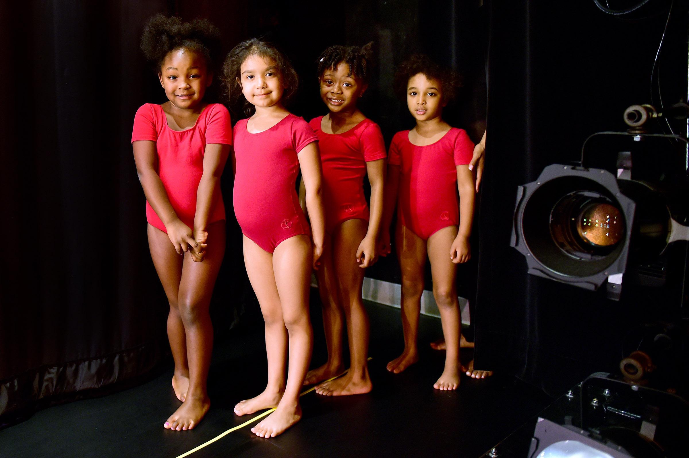 Four girls in red leotards stand backstage