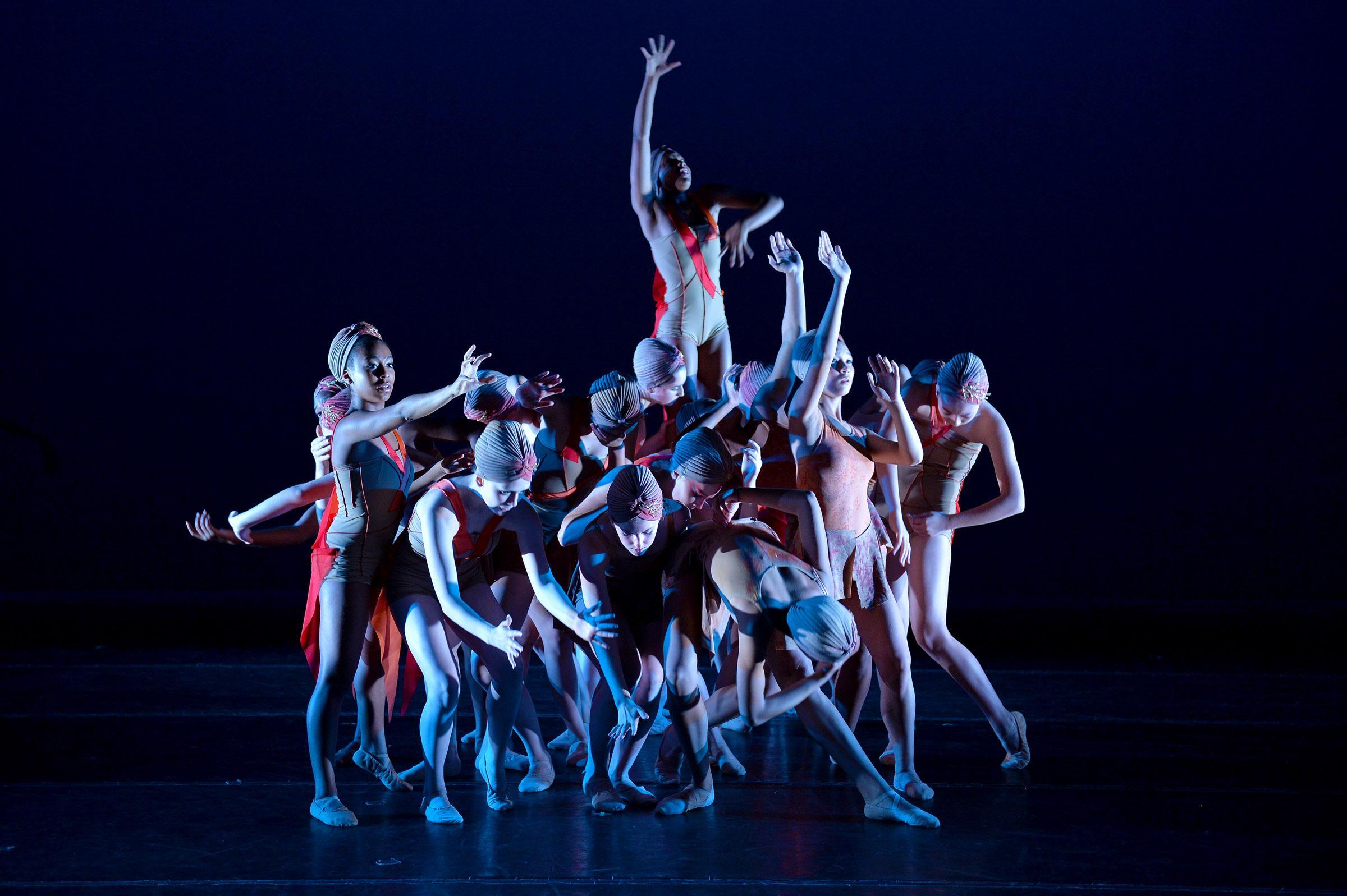 A group of dancers piled posing on stage in a huddle