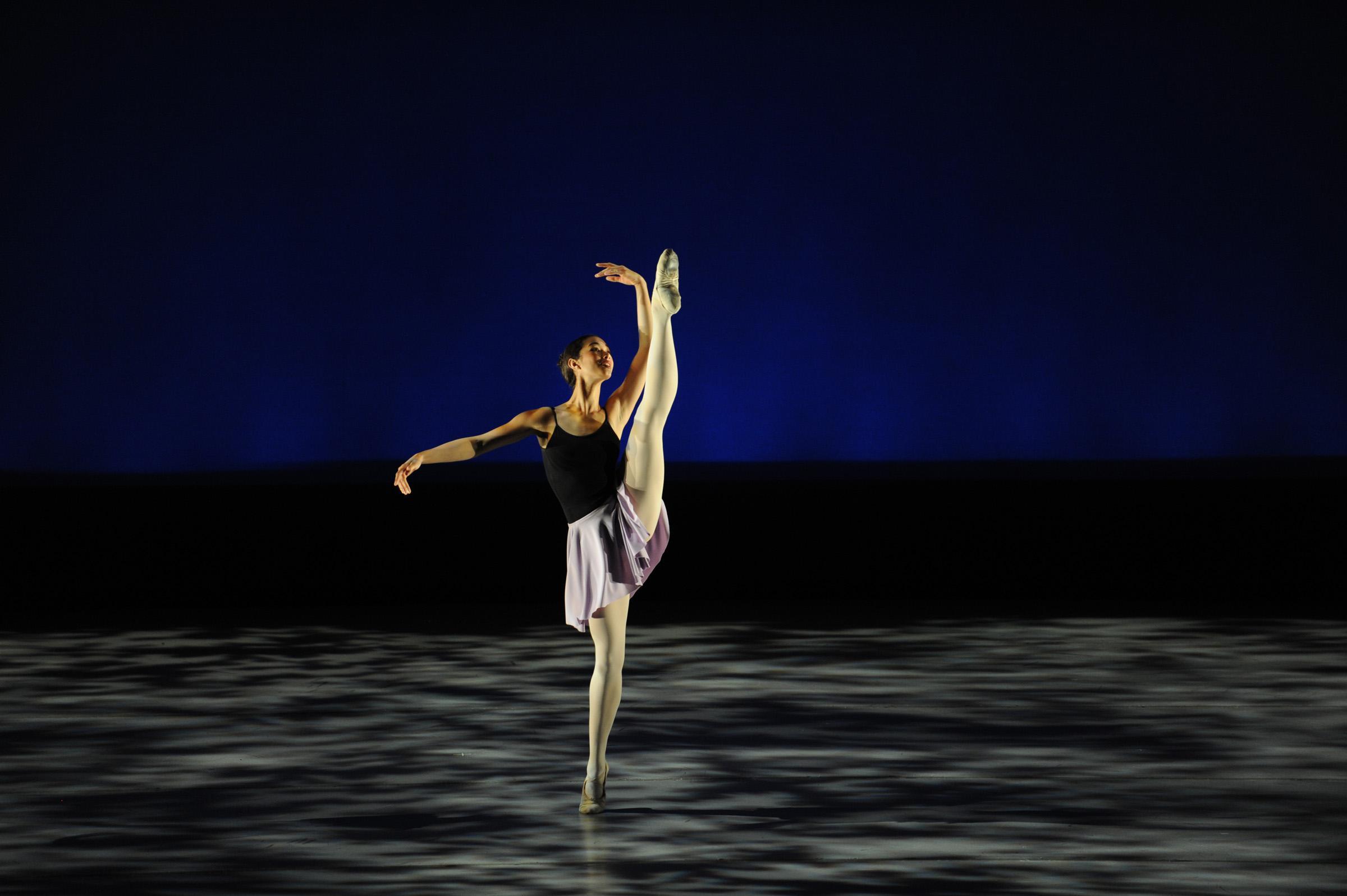 A dancer on stage in a leotard dress with one leg in the air