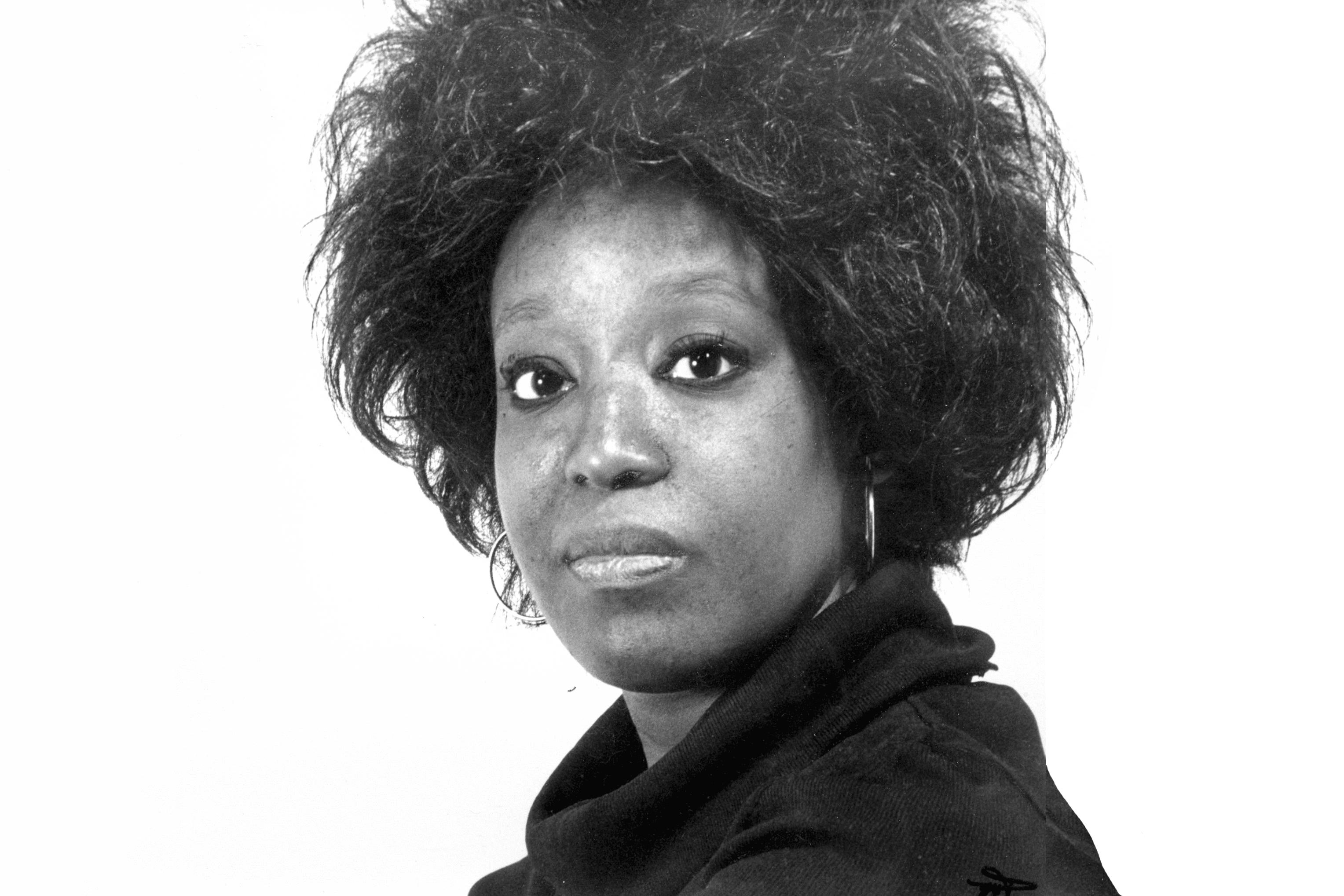 A black and white photo of Joan Peters. A black woman wearing hoop earrings and a turtle neck top.