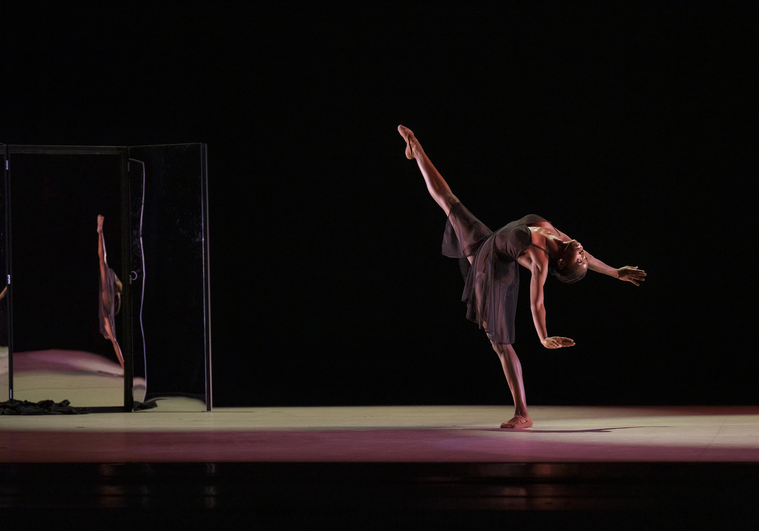 A woman in a black dress leans back kicking one leg up into the air.