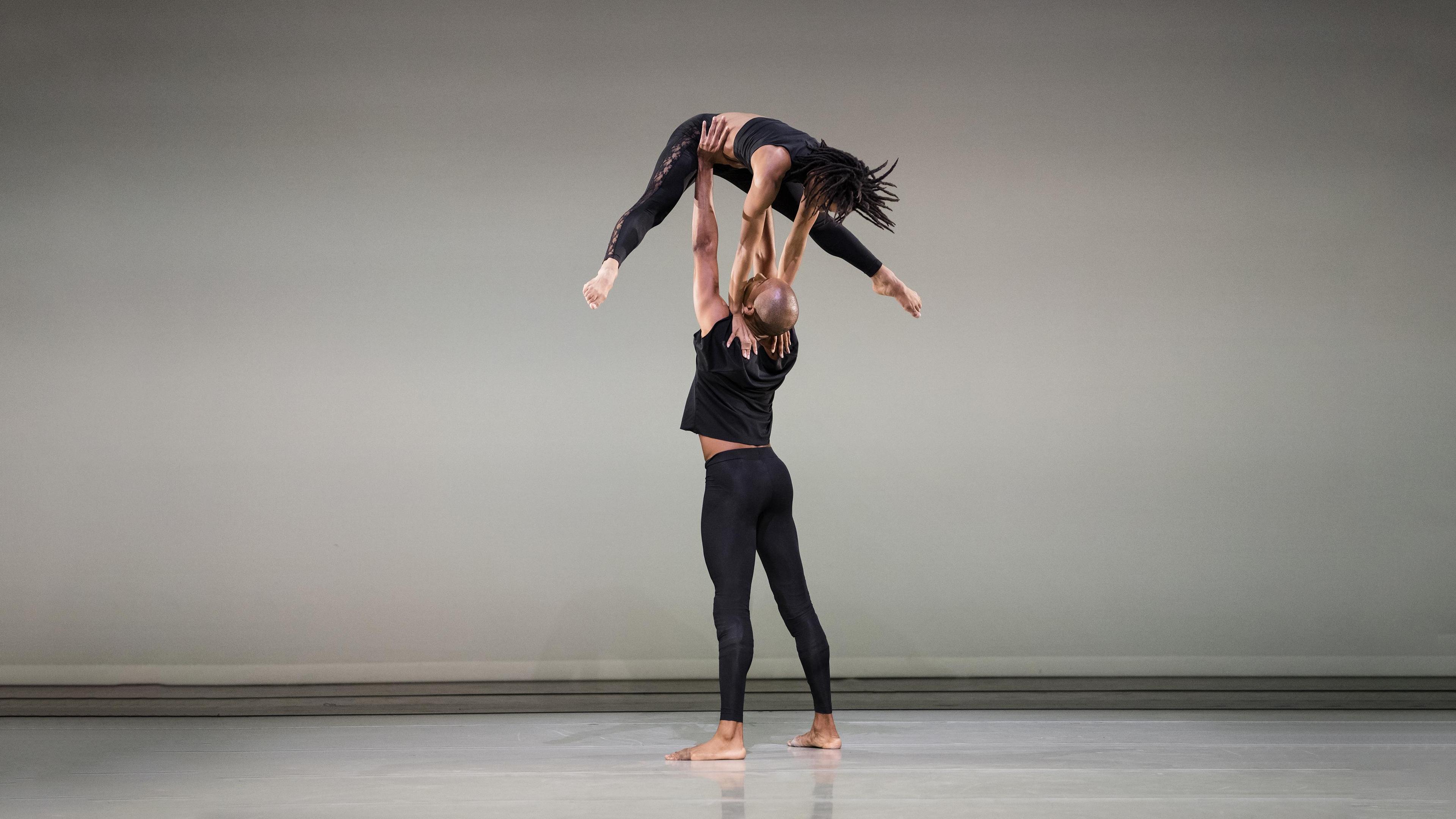 Bald dancer holding another dancer up above his head