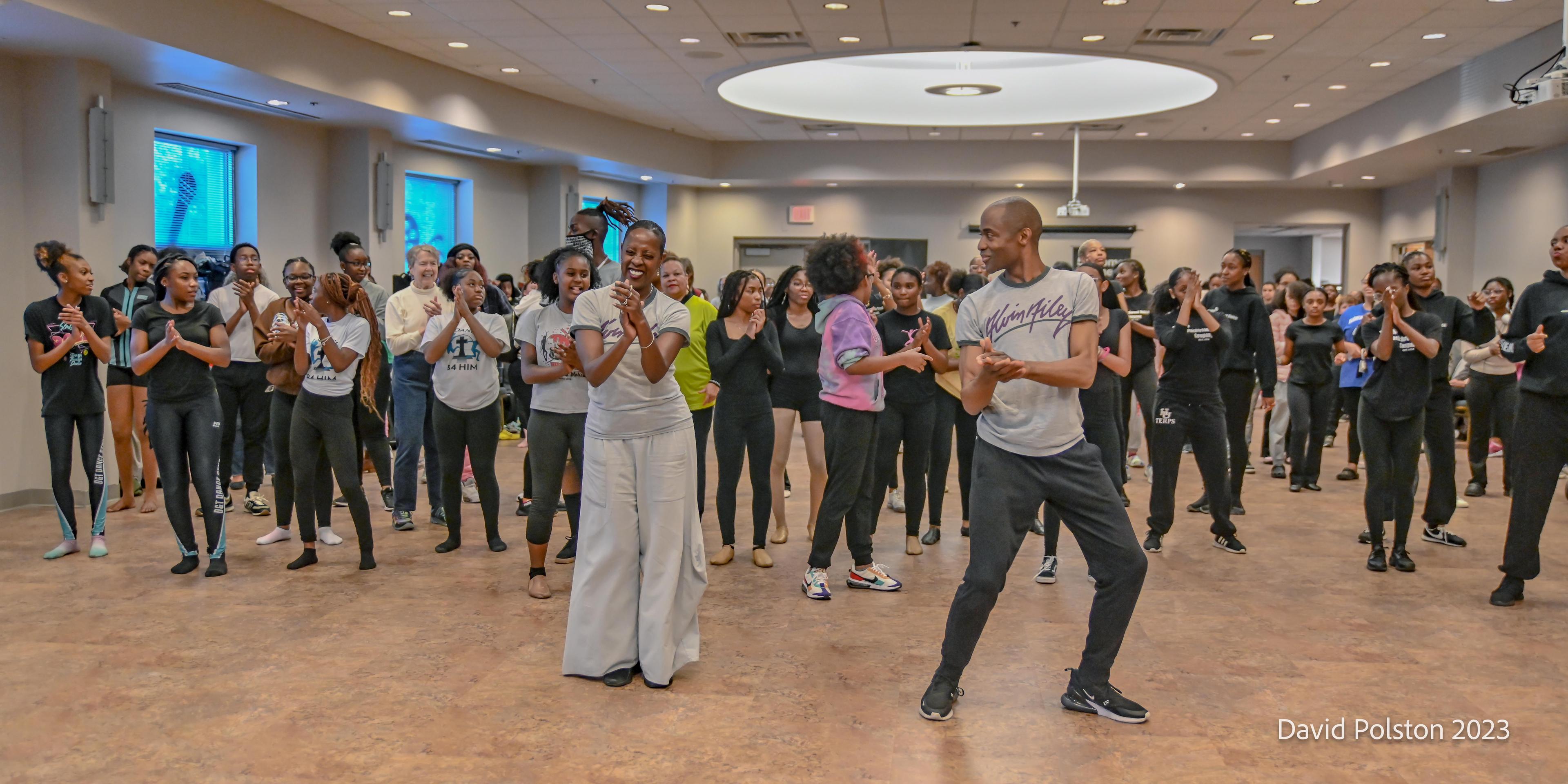 A male and female dance instructor lead a workshop for a group of people of all ages.