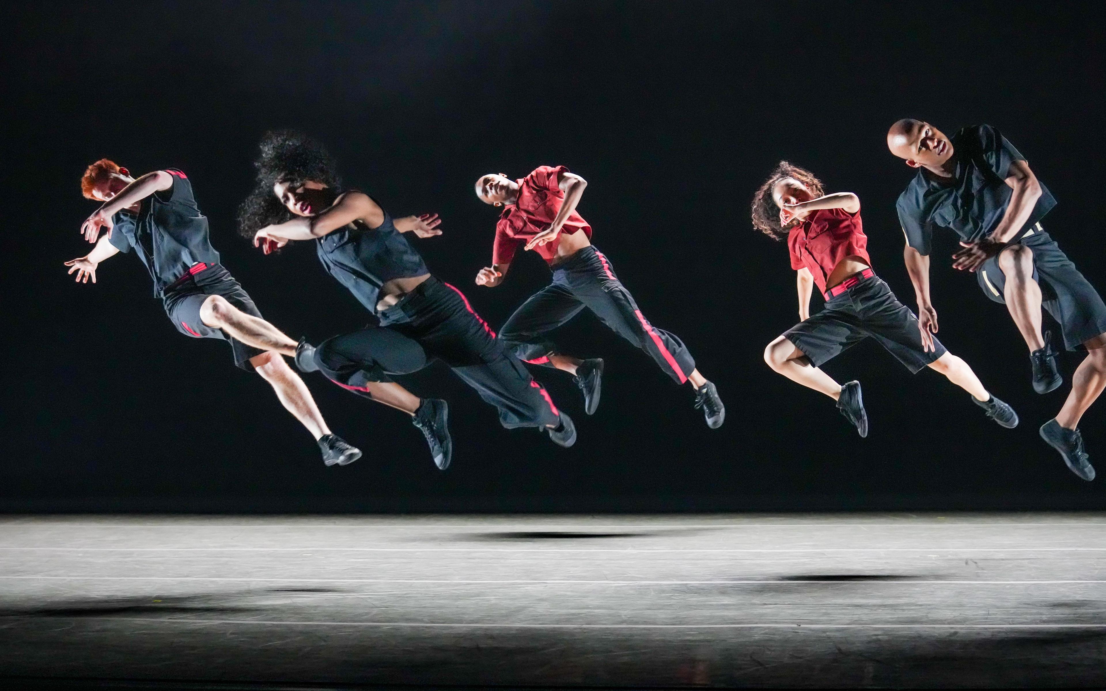 a group of dancers jump in the air all leaning at an angle to the ground.