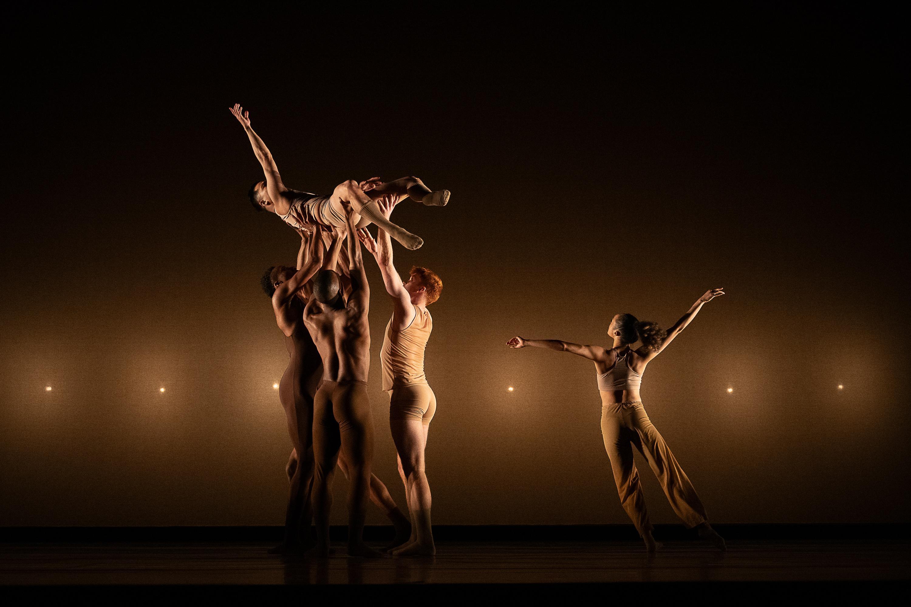 A group of dancers lift another dancer into the air.