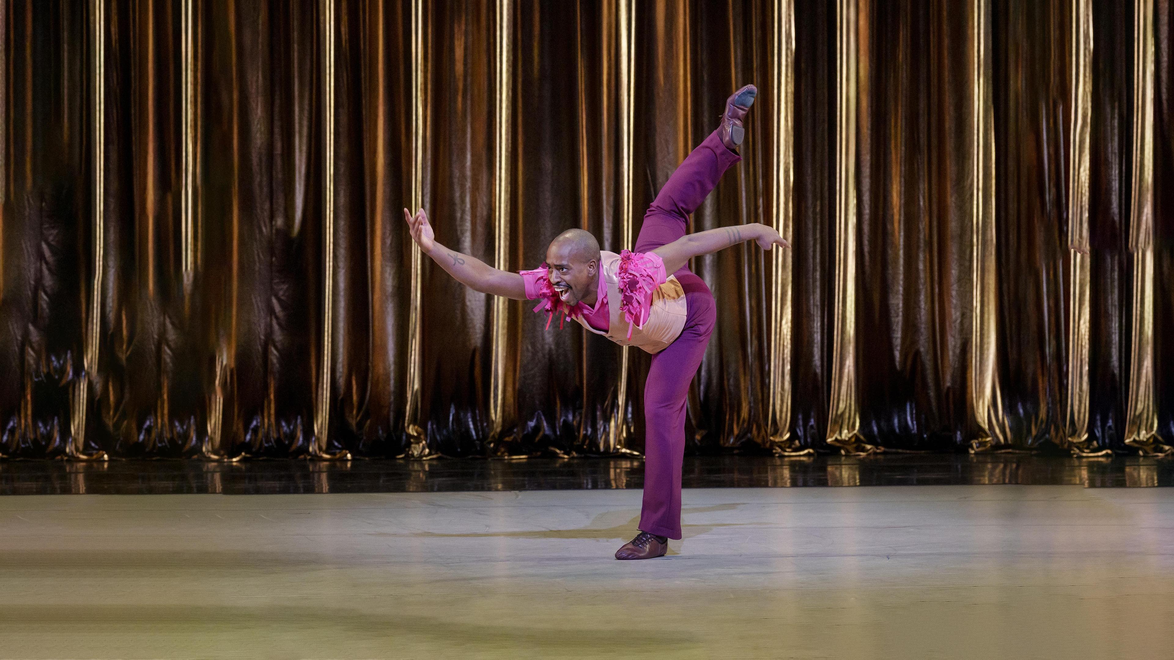 A man in a pink suit reaches foward with one arm as he kicks one leg back behind him.