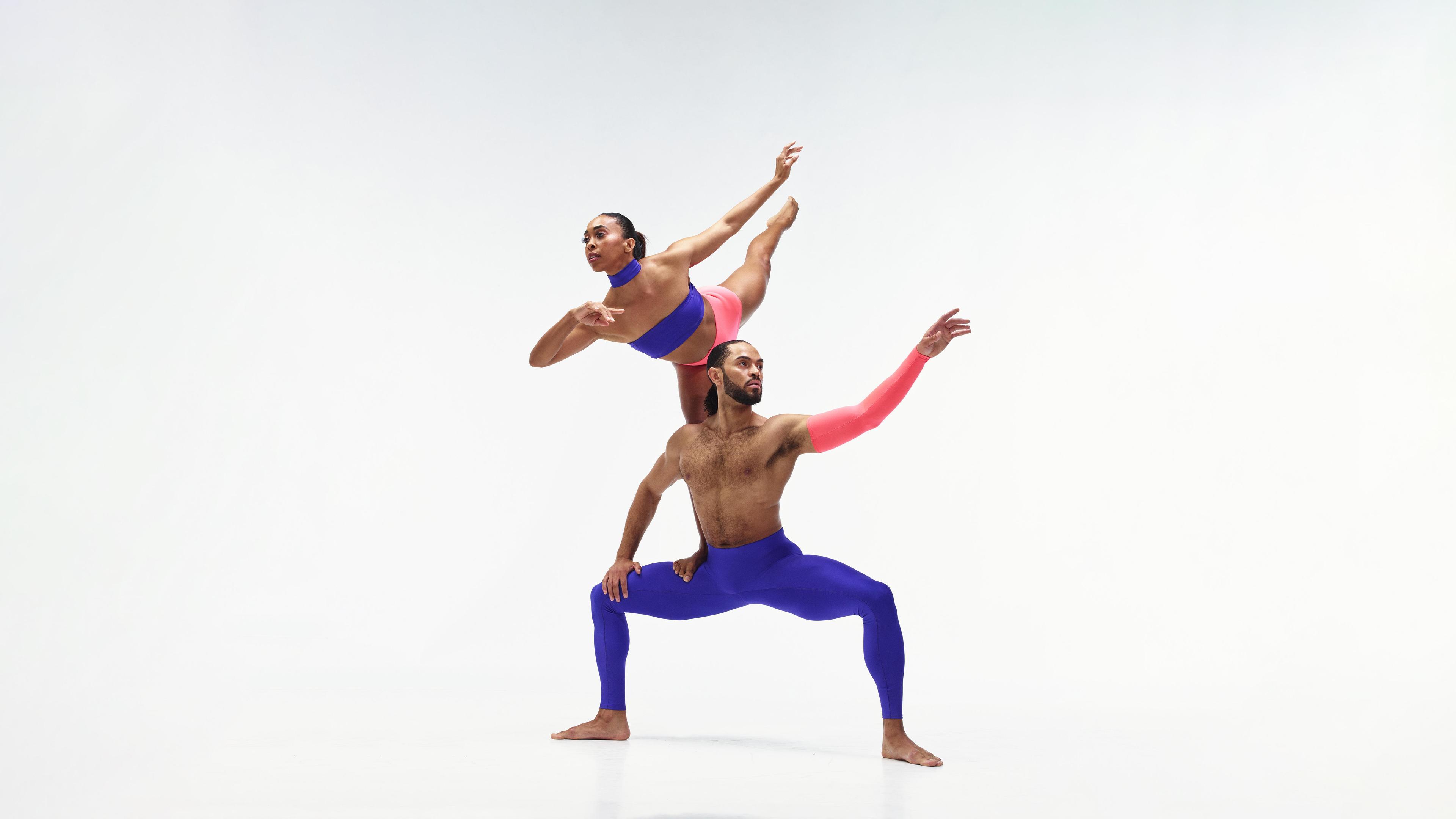 A female dancer is perched on the shoulders of a male dancer who stands with his legs bent