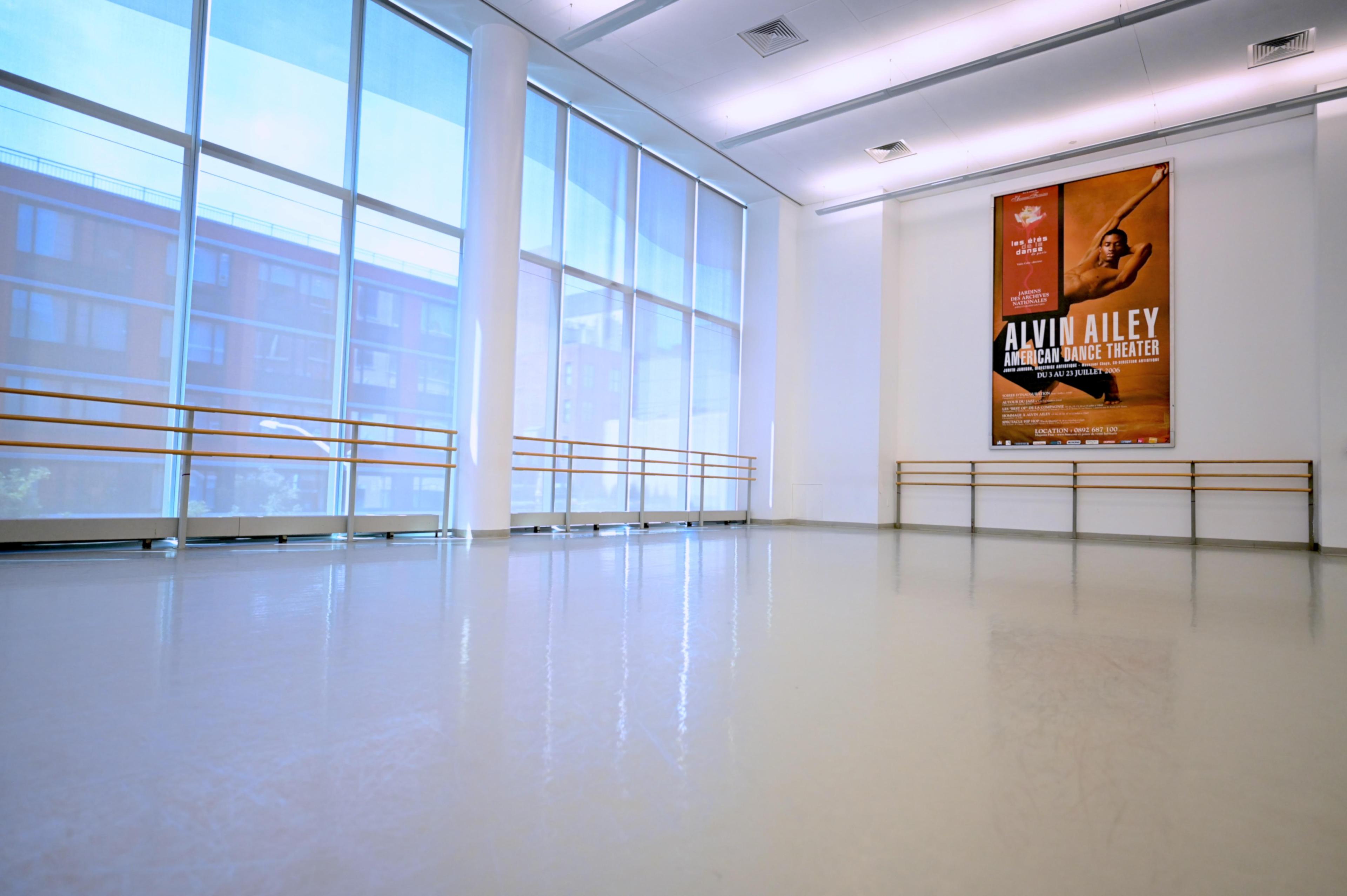 A dance studio with ballet barres, and windows along one wall