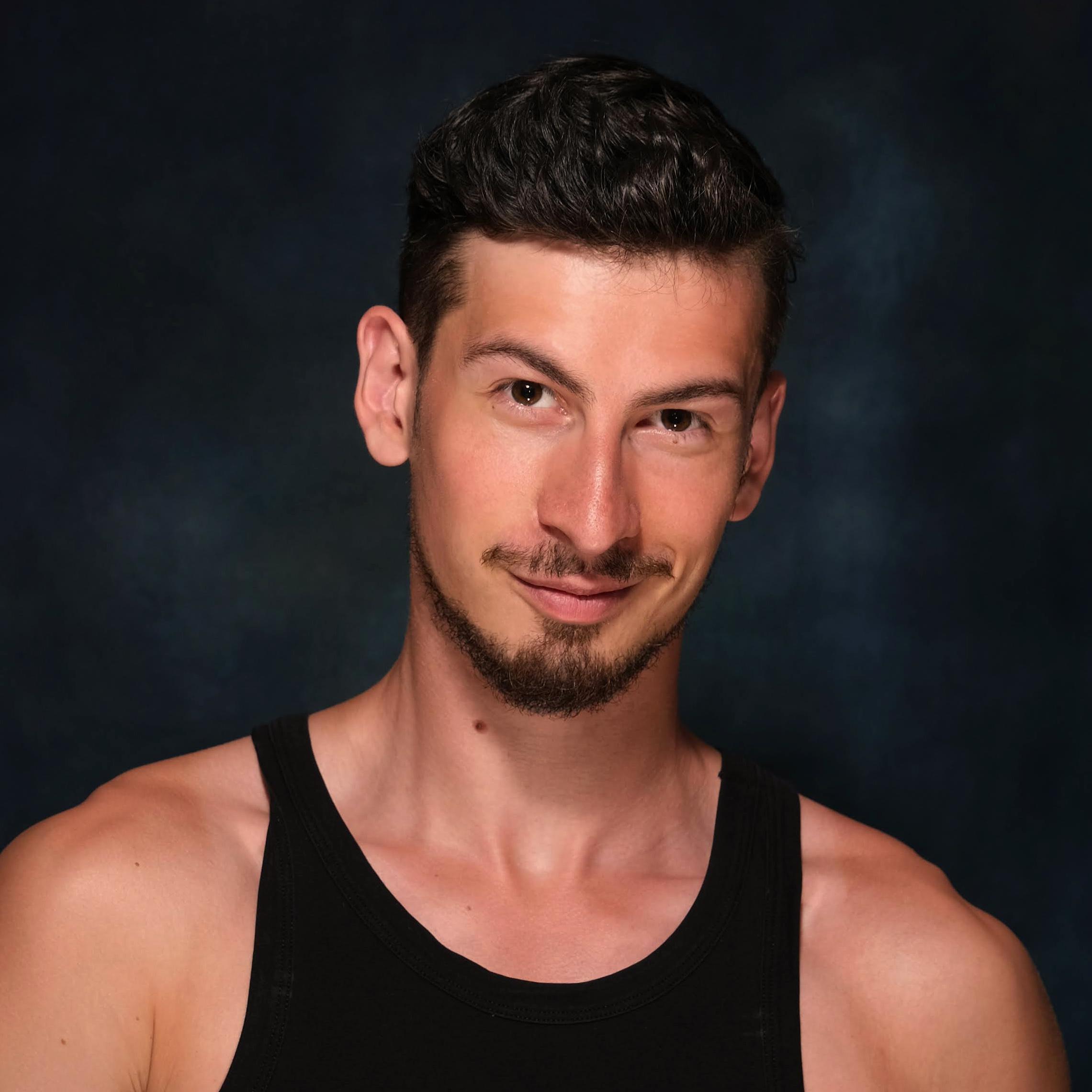 Headshot of a white man with brown hair and facial hair, and wearing a black tanktop