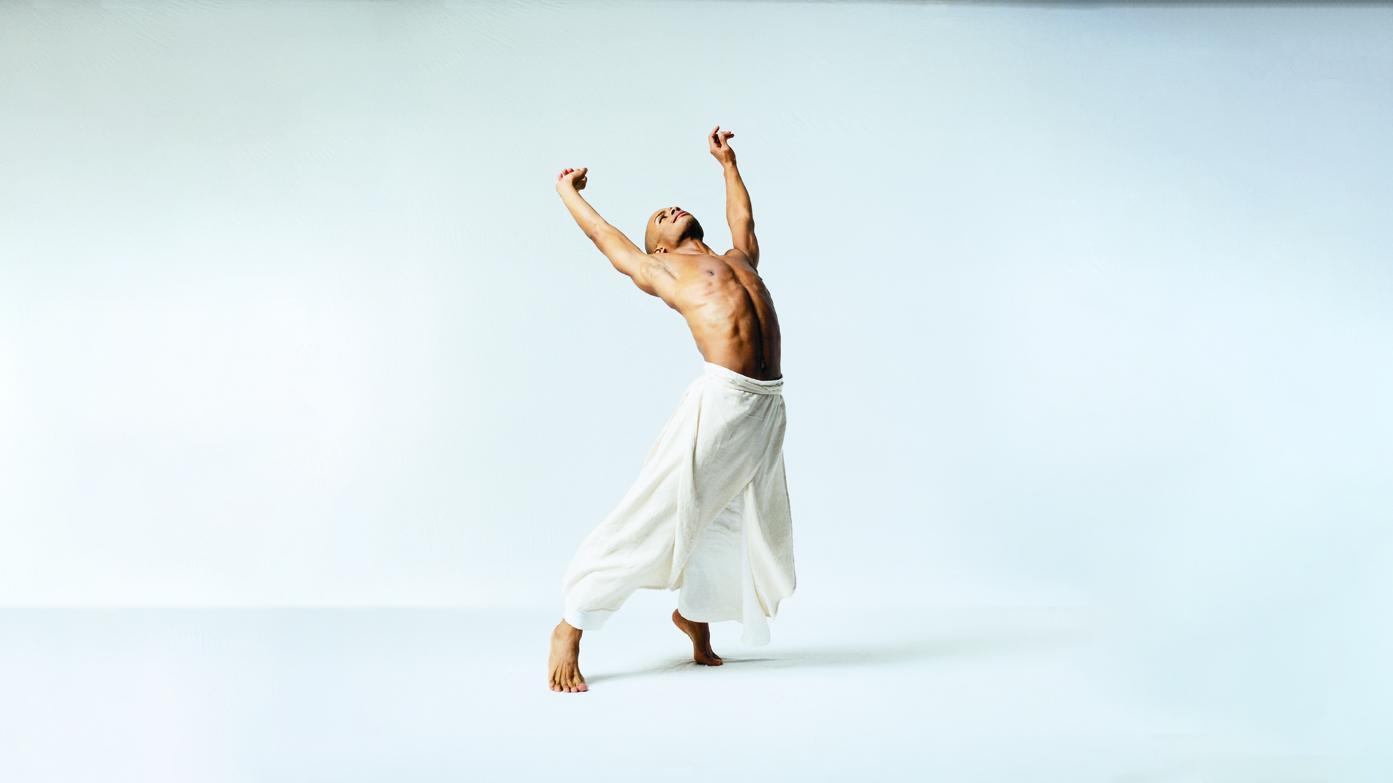 A shirtless man in billowing white pants reaches up to the sky