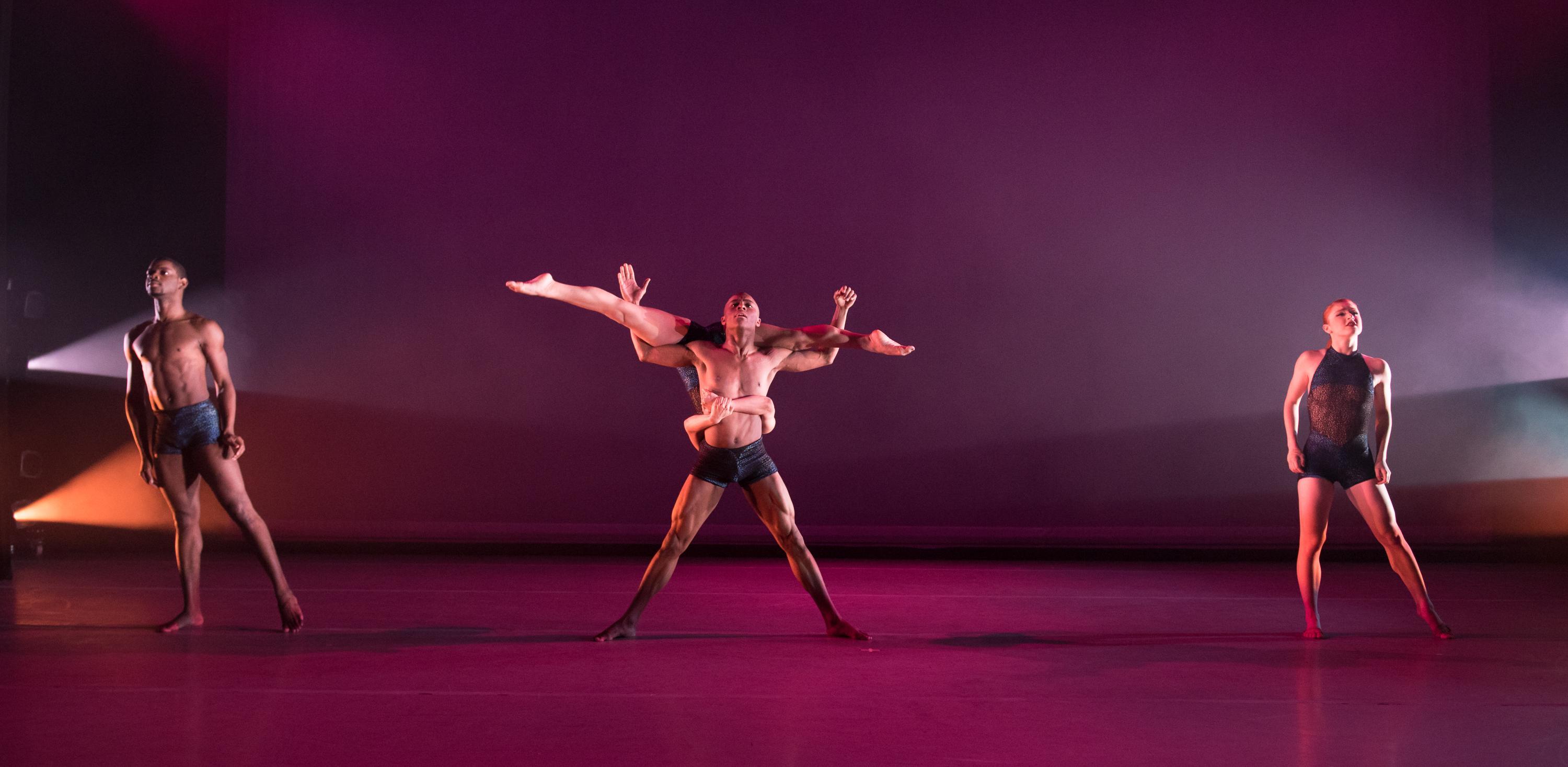 two dancers stand on either side of the stage and another two are in the middle with one dancer holding the other horizonatlly across his shoulders.