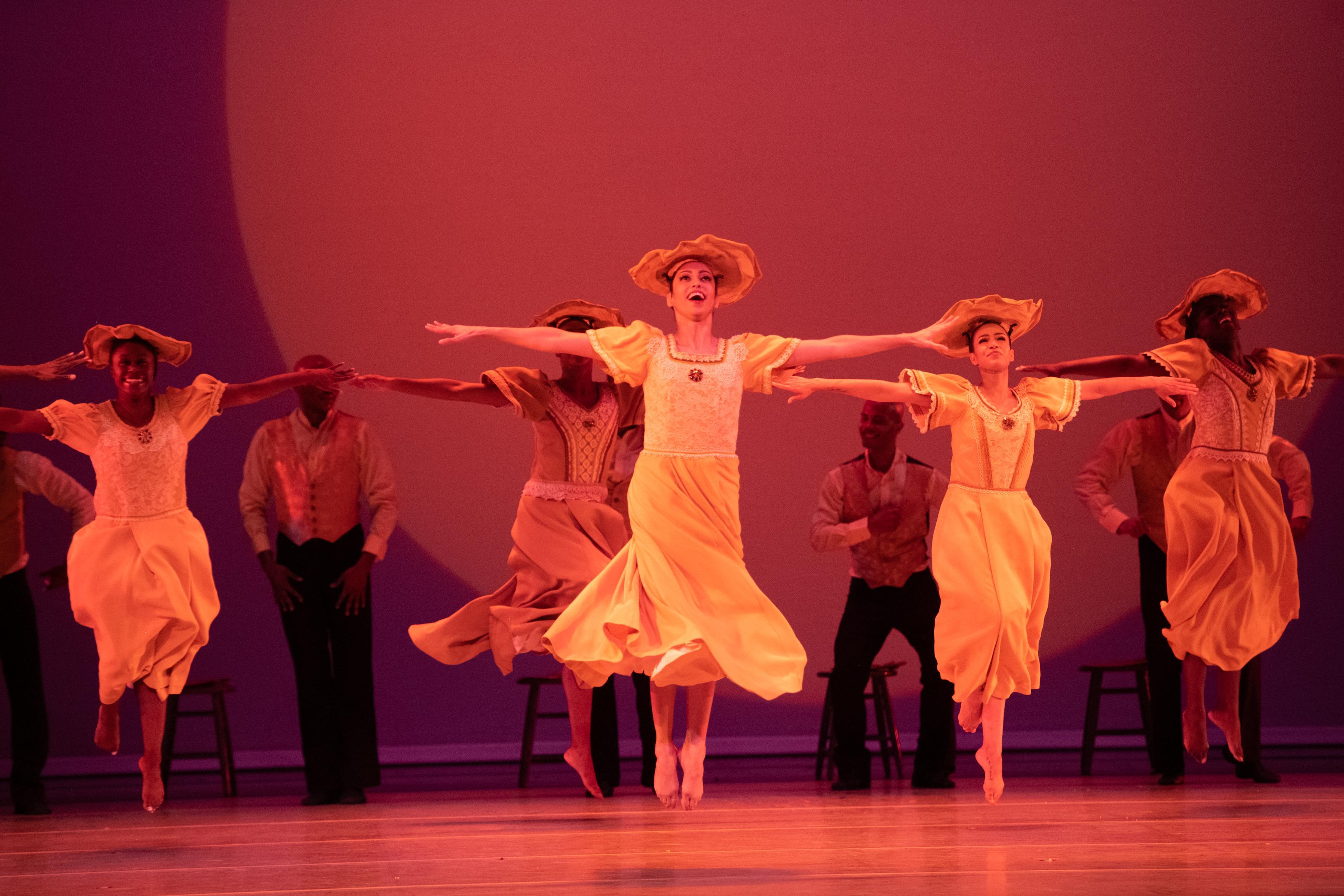 The Company jumping with straight legs and arms straight to the side in yellow