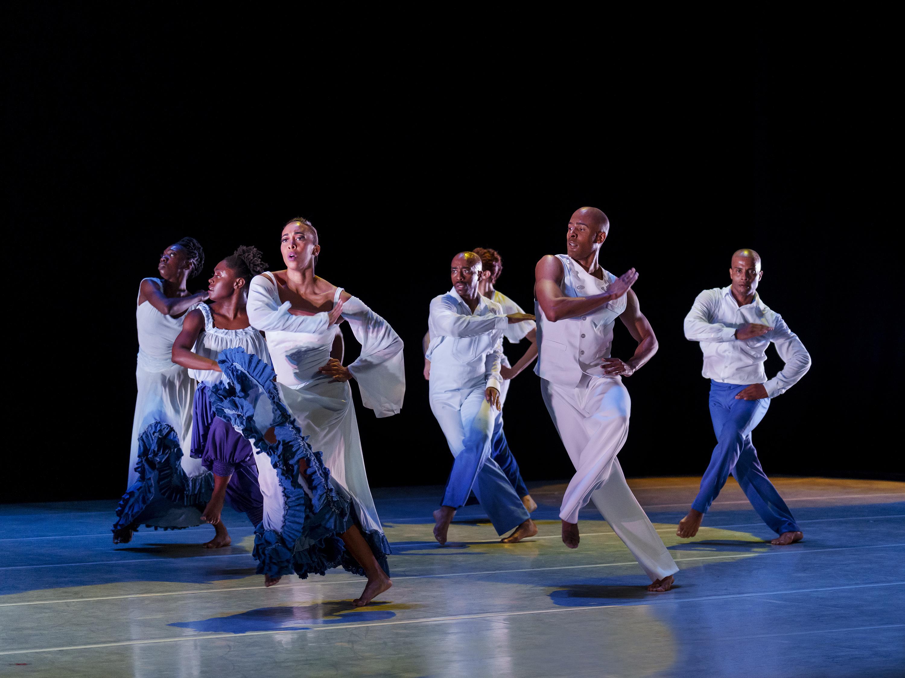 Members of the company all performing the same pose with one arm crossed over their chest and their other hand resting on their hips